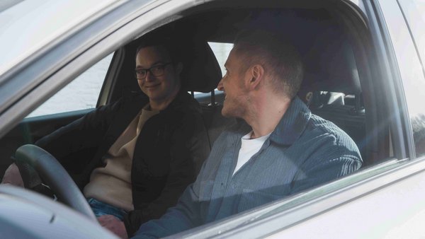 Ist ein Auto sinnvoll? Zwei junge Männer sitzen in einem Auto und lächeln sich an