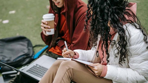 Deux étudiants assis sur une pelouse, étudiant ensemble.