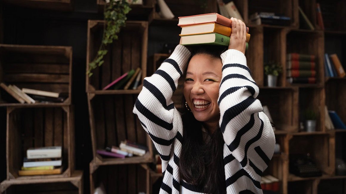 30 Prozent für Freizeit und persönliche Wünsche Frau mit gestreiftem Pullover hält lachend Bücher über ihren Kopf.