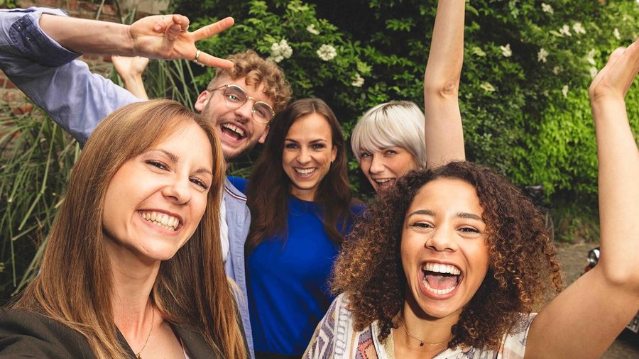 Urlaub mit Freunden planen – so geht’s Fünf Freunde stehen eng beieinander und lachen in die Kamera