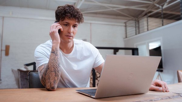 Hochwasser und Autos – Welche Versicherung zahlt? Junger Mann sitzt telefonierend vor einem Laptop.