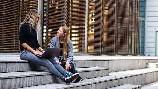 Studentinnen sitzen lachend auf einer Treppe 